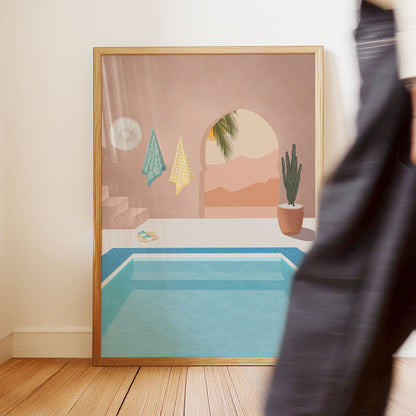 Framed artwork of a desert scene with a pool on a wall.