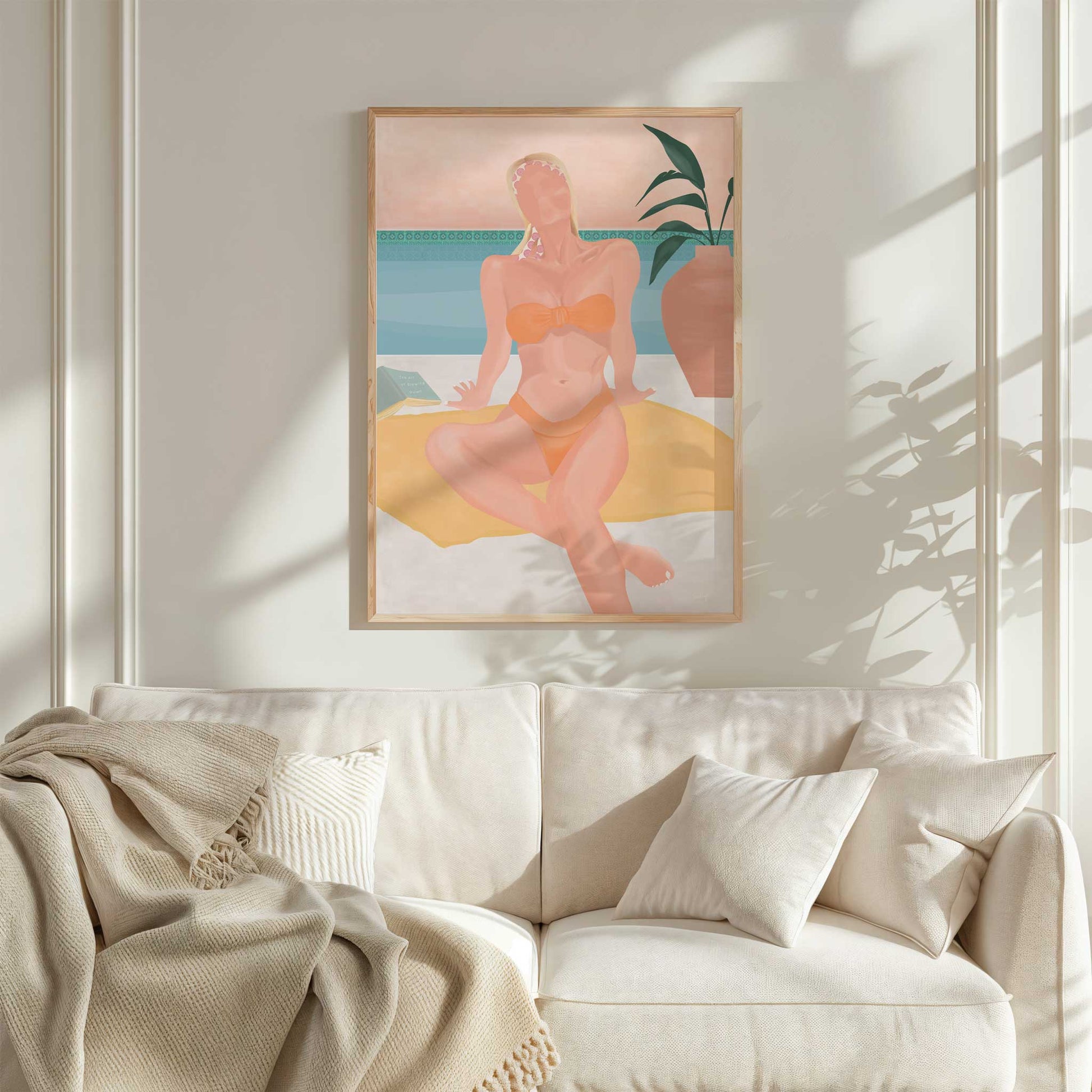 Framed artwork of a woman in a bikini on a beach, hanging above a white sofa.