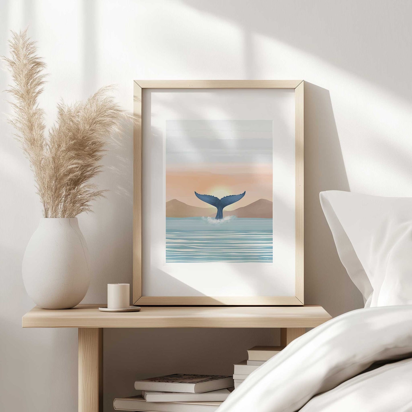 Framed artwork of a whale tail emerging from water on a bedside table.